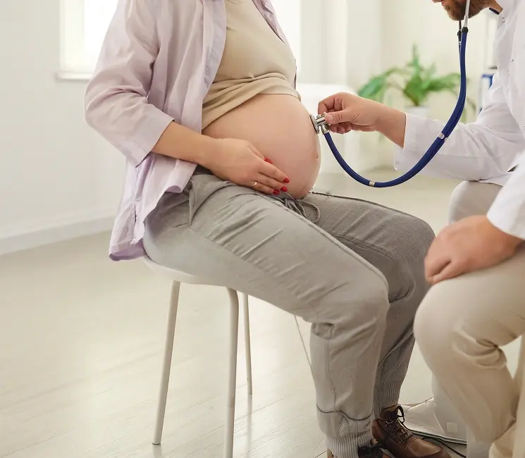 Doctor checking pregnant woman's abdomen with a stethoscope during routine prenatal examination